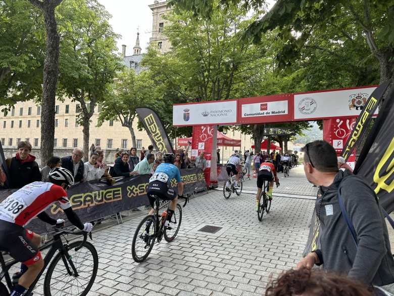 Cyclists crossing the finish line after a brutal uphill stretch in the 2023 Memorial David Montenegro cycling race in El Escorial.