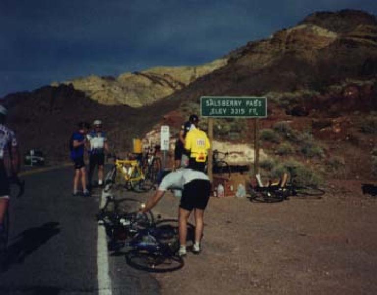 cyclists with bikes on the ground in front of Salsberry Pass Elevation 3315 sign.