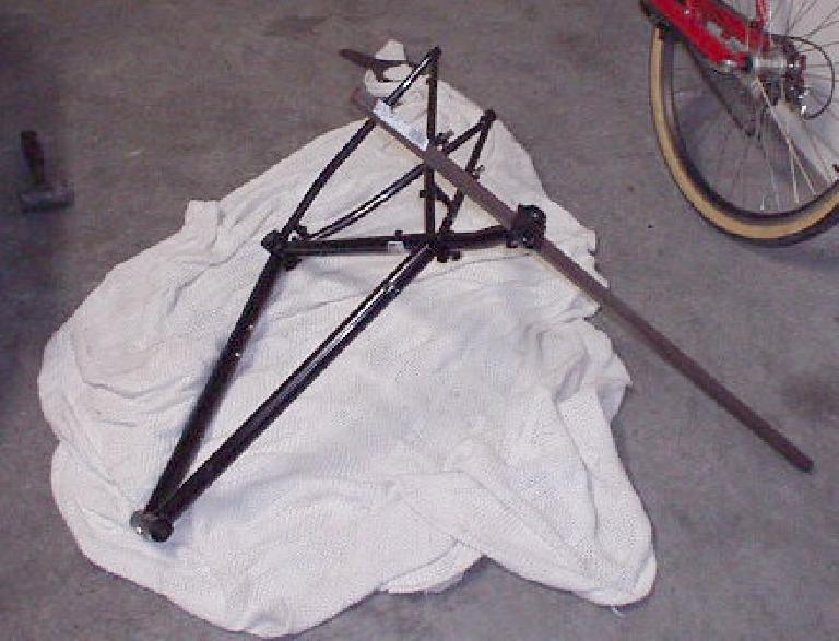black bike frame with stuck seatpost attached to a long steel bar on white towel
