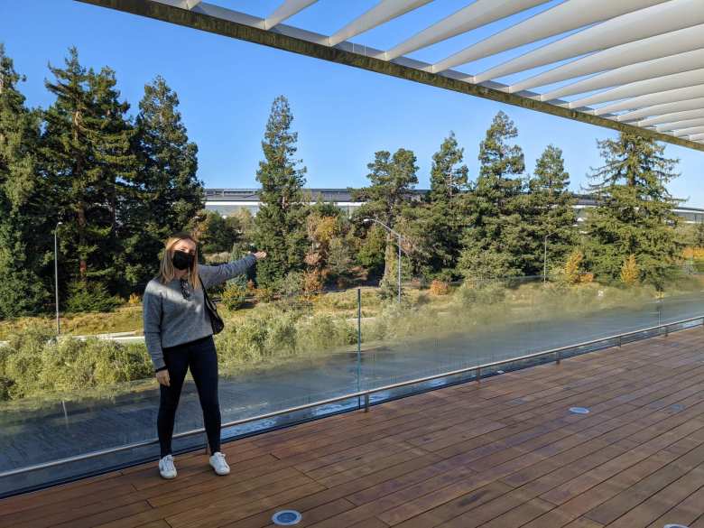 Andrea on the rooftop of the Apple Visitor Center, with arm pointing towards the Apple "Spaceship" headquarters.