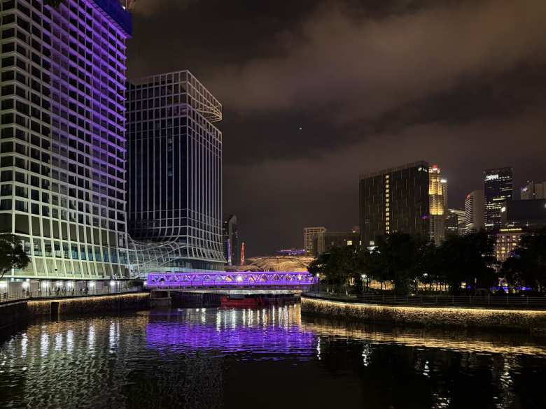 A bridge lighted in violet over the Singapore River at night.