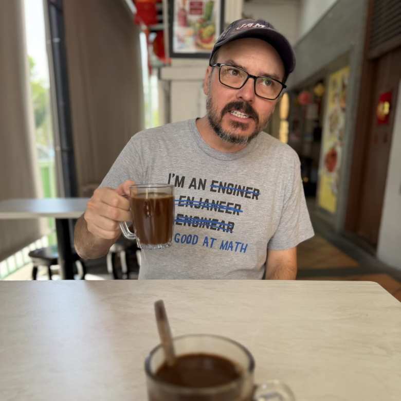 James with a cup of Kopi Siu Dai (a less sweet Kopi coffee), wearing an 