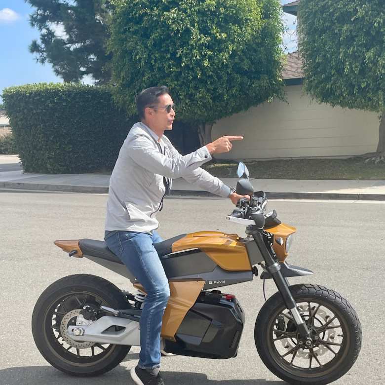 Felix pointing forward while sitting on a prototype of the Ryvid Anthem motorcycle.