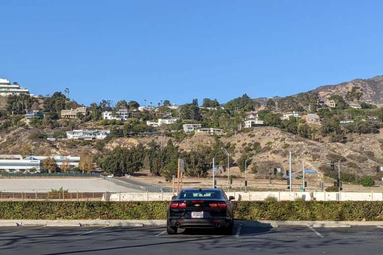 A black 2020 Chevrolet Camaro in a parking lot with large white homes in the hills of Malibu behind.