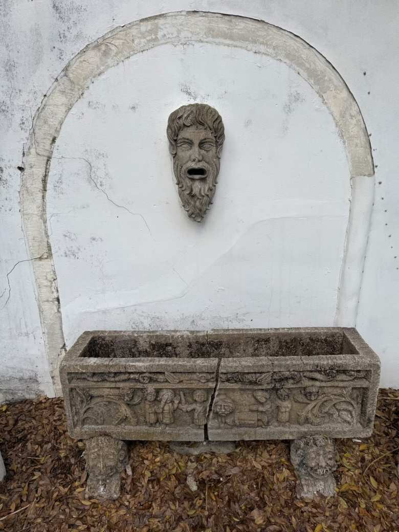 A stone carving of a bearded man on a white wall above a trough.