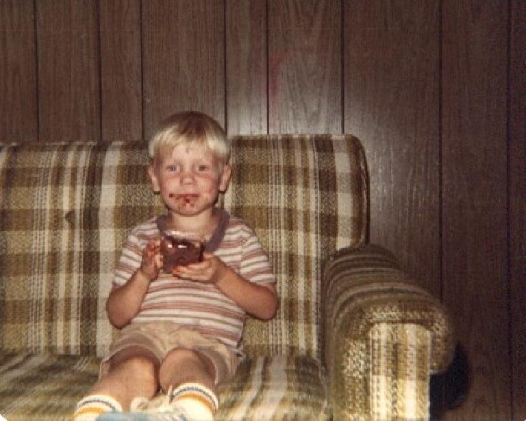 Photo: Stephen Cook in striped shirt on plaid sofa holding bowl and having chocolate smudge on his face.