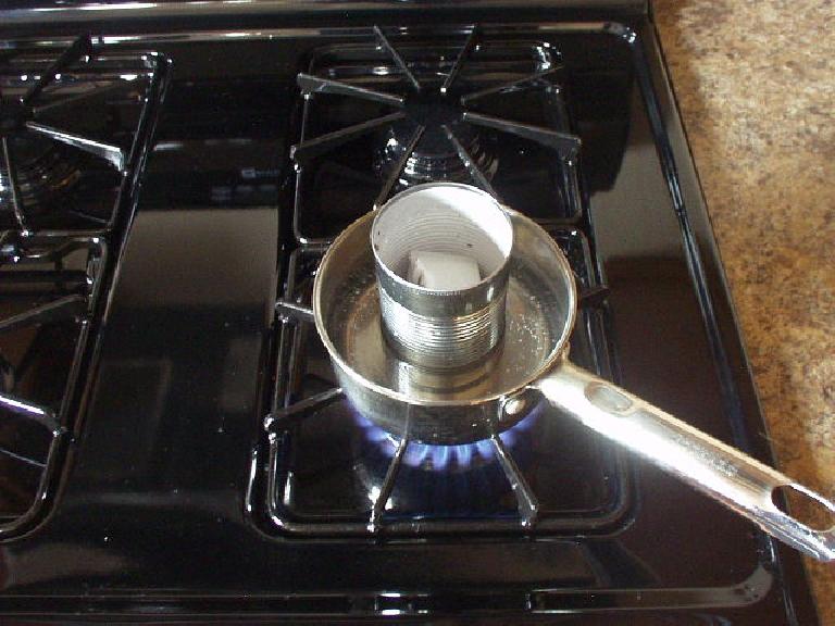 black gas stovetop with pot containing water and metal can of wax