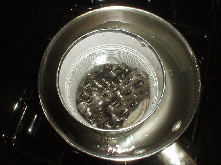 Melted wax and a bicycle chain inside a tin can inside a pot of boiling water.